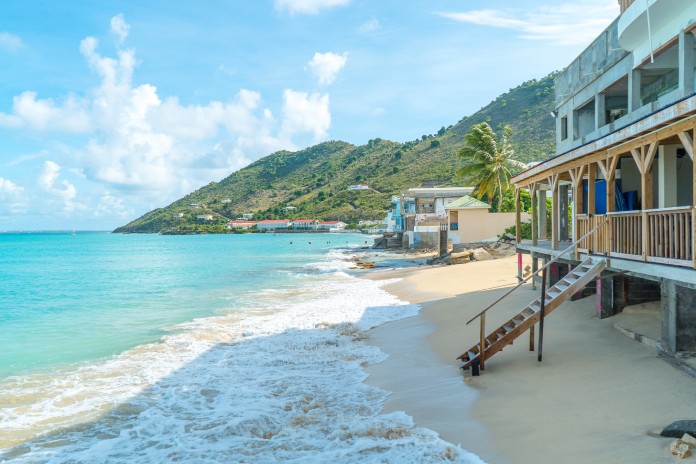 A beach house built on the sand in the Caribbean. The house has a wooden staircase leading down to the shoreline.