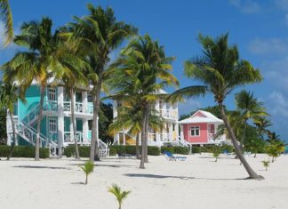 A row of colorful beach houses on the beach in the Caribbean with views of tall palm trees and white sands