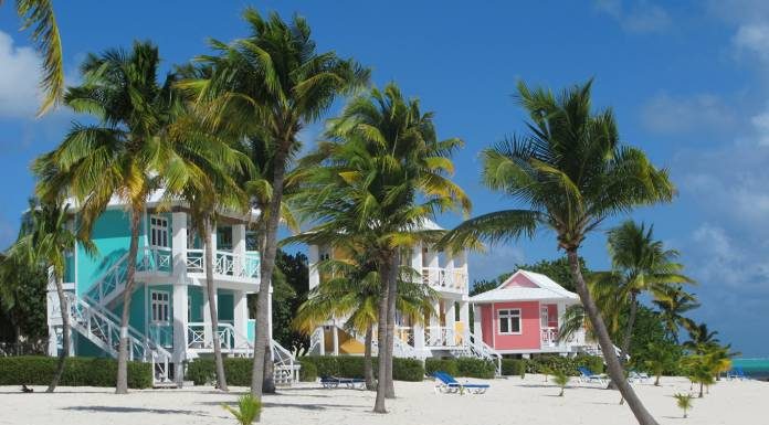 A row of colorful beach houses on the beach in the Caribbean with views of tall palm trees and white sands