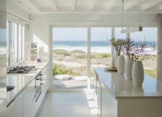 A beach house's beautiful kitchen. The space is painted white and features high-quality appliances and indoor plants.