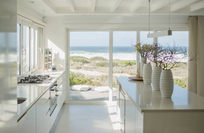 A beach house's beautiful kitchen. The space is painted white and features high-quality appliances and indoor plants.