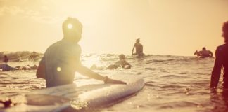 A group of people surfing in open waters beneath clear skies at sunrise. A gentle wave is coming toward them.