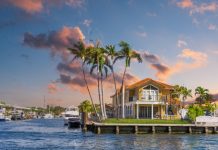 A beautiful, orange Florida home sits on a waterfront property. Palm trees scatter the landscaping.