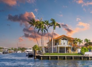 A beautiful, orange Florida home sits on a waterfront property. Palm trees scatter the landscaping.