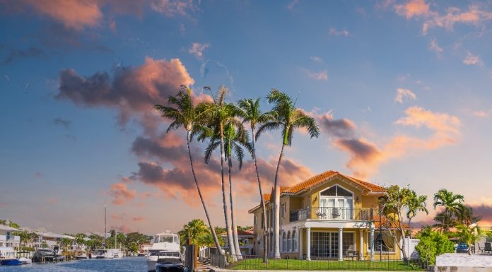 A beautiful, orange Florida home sits on a waterfront property. Palm trees scatter the landscaping.