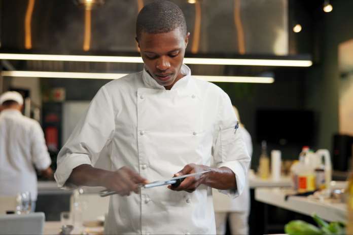 An African American chef sharpening a knife in a restaurant kitchen. Other chefs are in the background.