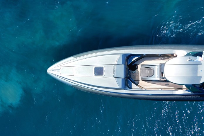 The deep-blue sea with a yacht vacation charter cruising through the waves. The charter is white with a roof and deck.