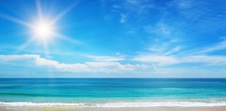 The crystal clear blue water splashes onto the white sandy beach. The sun shines bright in the blue sky.