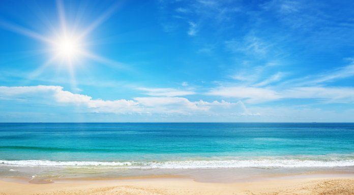 The crystal clear blue water splashes onto the white sandy beach. The sun shines bright in the blue sky.