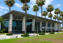 A large recreation center with top-to-bottom windows. There are a lot of palm trees in front of this building.