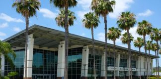 A large recreation center with top-to-bottom windows. There are a lot of palm trees in front of this building.