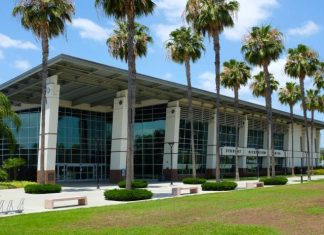 A large recreation center with top-to-bottom windows. There are a lot of palm trees in front of this building.