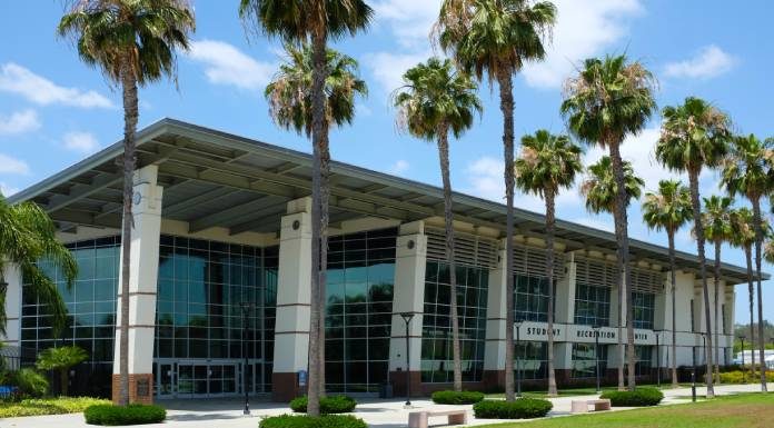 A large recreation center with top-to-bottom windows. There are a lot of palm trees in front of this building.