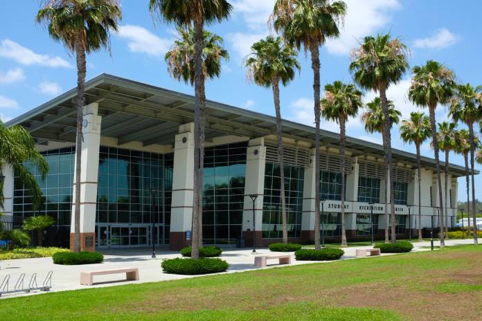 A large recreation center with top-to-bottom windows. There are a lot of palm trees in front of this building.