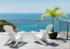 Two white beach chairs sit on a wooden desk next to a potted Caribbean plant. The deck overlooks the ocean.