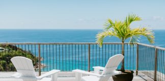 Two white beach chairs sit on a wooden desk next to a potted Caribbean plant. The deck overlooks the ocean.