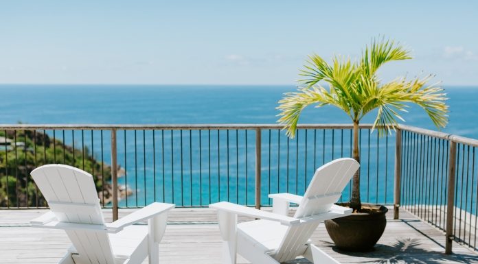 Two white beach chairs sit on a wooden desk next to a potted Caribbean plant. The deck overlooks the ocean.