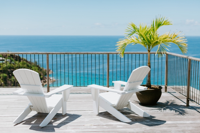 Two white beach chairs sit on a wooden desk next to a potted Caribbean plant. The deck overlooks the ocean.