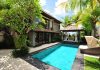 A villa with a pool, lounging chairs, and palm trees. It's a sunny day with a few clouds in the sky.