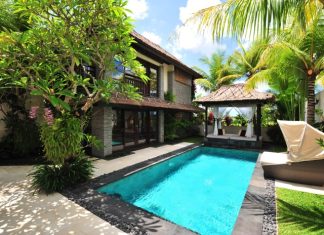 A villa with a pool, lounging chairs, and palm trees. It's a sunny day with a few clouds in the sky.