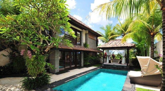 A villa with a pool, lounging chairs, and palm trees. It's a sunny day with a few clouds in the sky.