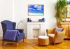 A living room with fireplace mantel featuring blue decorations, blue wingback chair, and wicker chair with matching ottoman.