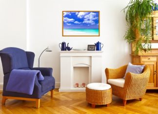 A living room with fireplace mantel featuring blue decorations, blue wingback chair, and wicker chair with matching ottoman.