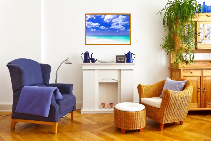 A living room with fireplace mantel featuring blue decorations, blue wingback chair, and wicker chair with matching ottoman.