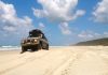 An off-road vehicle on the beach going for a cruise. There is a luggage rack on the top with a hardcase luggage holder.