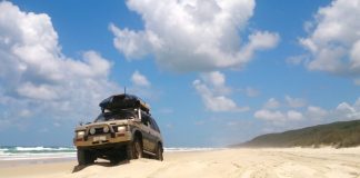 An off-road vehicle on the beach going for a cruise. There is a luggage rack on the top with a hardcase luggage holder.