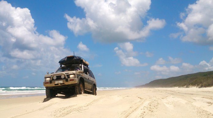 An off-road vehicle on the beach going for a cruise. There is a luggage rack on the top with a hardcase luggage holder.