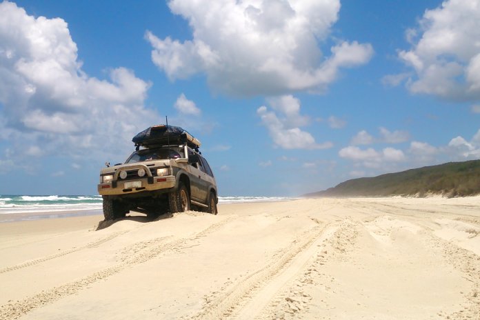 An off-road vehicle on the beach going for a cruise. There is a luggage rack on the top with a hardcase luggage holder.