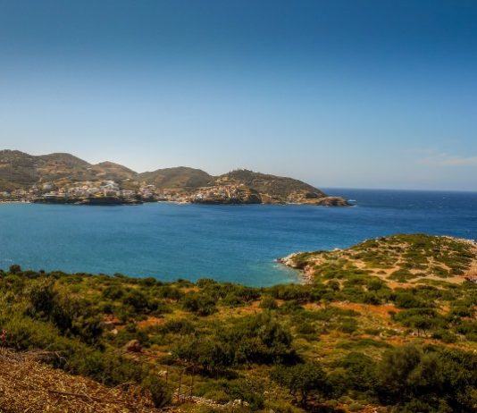 A view of an ocean from a raised spot on the land of an island. There are humanmade structures visible across the inlet.