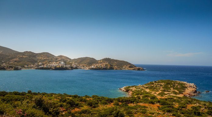 A view of an ocean from a raised spot on the land of an island. There are humanmade structures visible across the inlet.