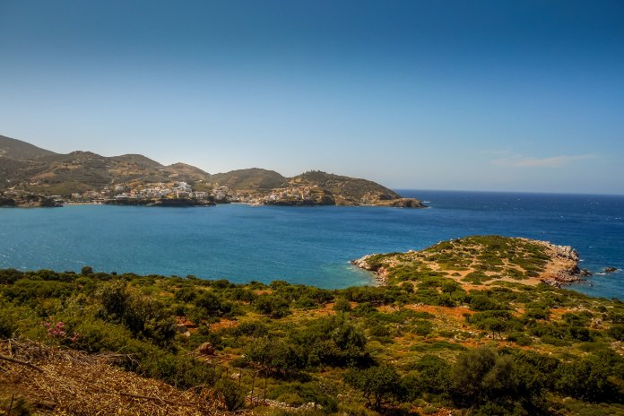 A view of an ocean from a raised spot on the land of an island. There are humanmade structures visible across the inlet.