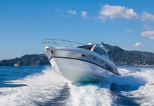 A sport motor boat making a sharp, fast turn on the ocean. There is a tropical, lush island behind the boat.