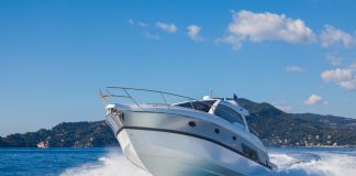 A sport motor boat making a sharp, fast turn on the ocean. There is a tropical, lush island behind the boat.