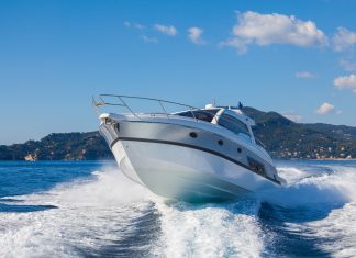 A sport motor boat making a sharp, fast turn on the ocean. There is a tropical, lush island behind the boat.