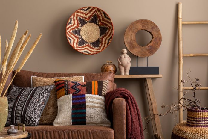 An interior design display of cultural living room decor with colorful pillows, a brown sofa, a wooden bench, and wall decor.