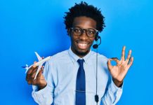 A young man wears a headset, holds a toy airplane in one hand, and uses his forefinger and thumb to create an "o" symbol.