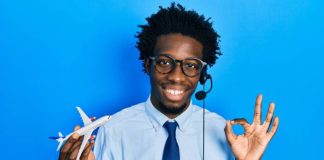 A young man wears a headset, holds a toy airplane in one hand, and uses his forefinger and thumb to create an "o" symbol.