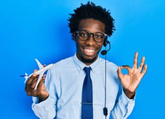 A young man wears a headset, holds a toy airplane in one hand, and uses his forefinger and thumb to create an "o" symbol.