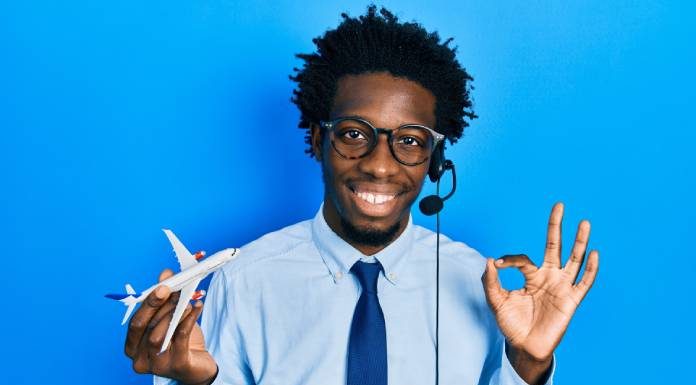 A young man wears a headset, holds a toy airplane in one hand, and uses his forefinger and thumb to create an "o" symbol.