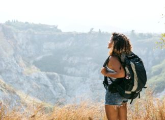Top Safety Tips for Solo Travelers in the Caribbean A young woman in shorts and a sleeveless top carries a backpack while looking out over a mountain landscape.