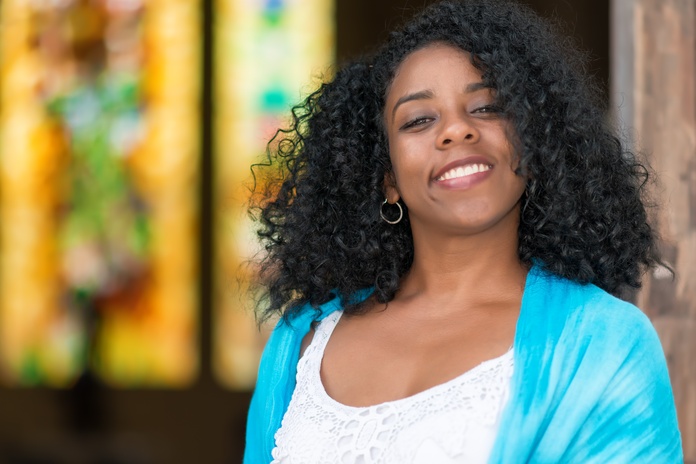 A young Black woman leans against a doorway, smiling happily. Her healthy hair gracefully falls to her shoulders. A young Black woman leans against a doorway, smiling happily. Her healthy hair gracefully falls to her shoulders.
