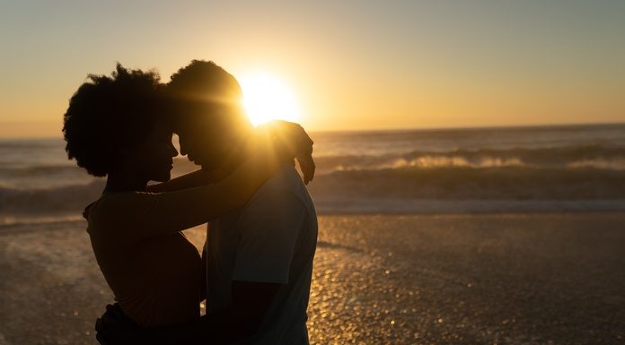 Caribbean Wedding Traditions To Inspire Your Big Day A joyful Black newlywed couple embraces each other during the golden hour as the sun sets on the beach.