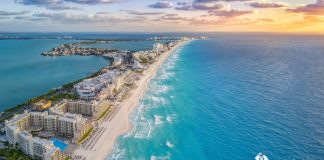 Tips for Breaking Into the Caribbean Travel Market An overhead view of an island in the Caribbean with buildings along the shore and a boat moving through blue water.
