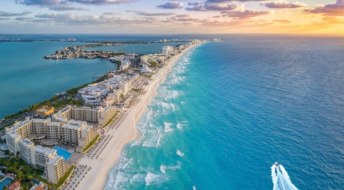 An overhead view of an island in the Caribbean with buildings along the shore and a boat moving through blue water.
