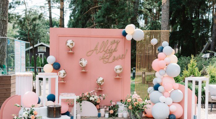 A detailed photo backdrop with pink accents, suitcases, globes, and various balloons. The backdrop says "all you need is love!"