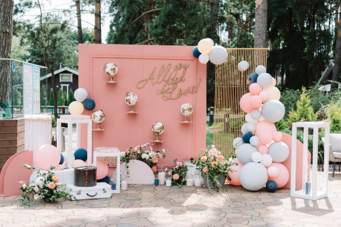 A detailed photo backdrop with pink accents, suitcases, globes, and various balloons. The backdrop says 